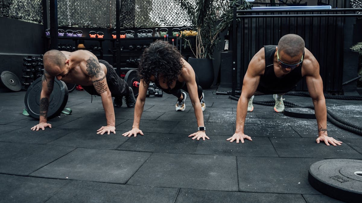 Three individuals performing push-ups together in a Mexico City gym setting.